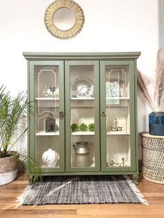 a green china cabinet sitting on top of a wooden floor next to a potted plant