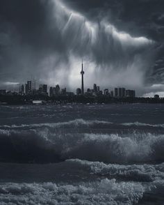 storm clouds loom over the city skyline in this black and white photo from across the ocean