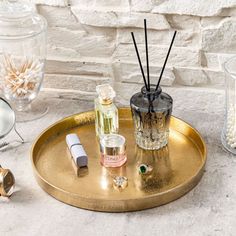 a gold tray with candles, perfume bottles and other items on it next to a white brick wall