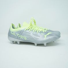 a soccer shoe with neon yellow laces on the bottom and white soles, against a gray background