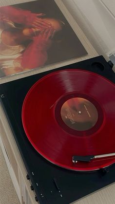 a red record player sitting on top of a white table next to a cd case