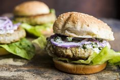 two burgers with lettuce, onions and cheese on them sitting on a wooden table