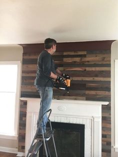 a man standing on a stepladder in front of a fireplace holding a drill