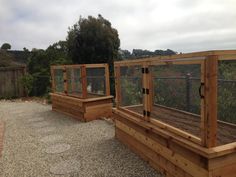 three wooden raised garden beds on gravel area next to fenced in area with trees