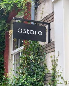 a black sign hanging from the side of a building next to a green plant covered wall