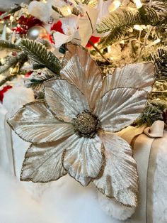 a christmas tree decorated with silver and white flowers, ornaments and lights in the background