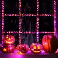 three pumpkins are lit up in front of a window with halloween decorations on it