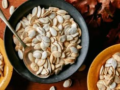 two bowls filled with pumpkin seeds and one bowl full of pumpkin seeds next to some leaves