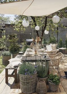 an outdoor dining area with wicker furniture and hanging lanterns above the table, surrounded by potted plants