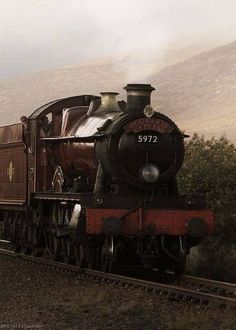 an old fashioned steam train traveling down the tracks in front of some trees and mountains