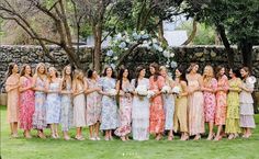 a group of women standing next to each other in front of a stone wall and trees