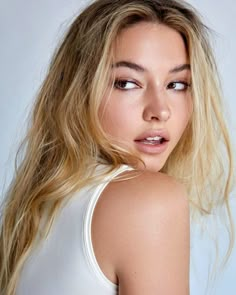 a woman with long blonde hair is posing for a magazine cover shot, wearing a white tank top