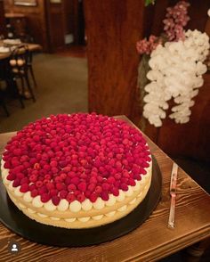 a cake with red and white toppings on a black platter next to flowers