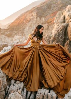 a woman is standing on some rocks with her dress blowing in the wind and mountains behind her