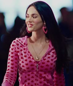 a woman with long black hair wearing a pink polka dot shirt and large hoop earrings