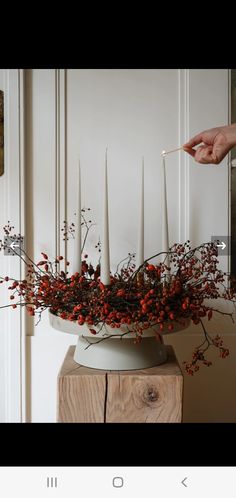 someone is lighting candles in a vase with red berries and greenery on the table