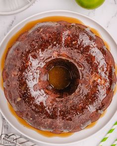 a chocolate cake on a plate with caramel sauce and two green apples in the background