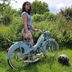 a woman standing next to a blue bike on top of a lush green field covered in grass