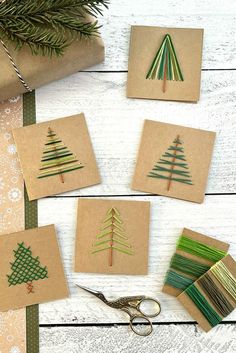 four christmas trees made out of brown paper on top of a white wooden table next to scissors