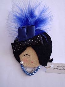 a small doll with a blue hat and pearls on it's head is next to a tag