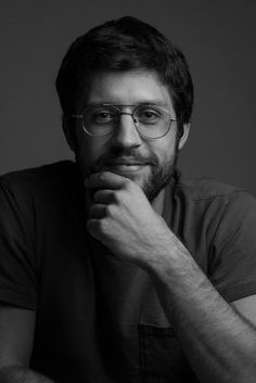 a black and white photo of a man in glasses looking at the camera with his hand on his chin