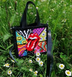 a cross - stitch purse sitting in the grass with daisies