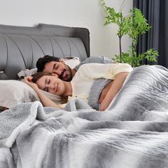 a man and woman laying in bed under a gray blanket with white sheets on it