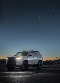 a white suv parked on the side of a road under a night sky filled with stars