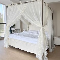 a large white bed sitting in a bedroom next to a window with curtains on it