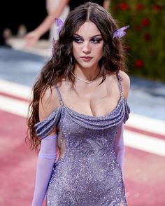 a model walks down the runway in a purple dress with long gloves on her head