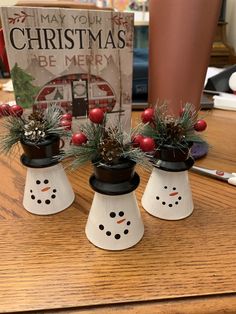 three snowmen with christmas decorations on their heads sitting on a table next to a book