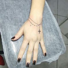 a woman's hand with a cross tattoo on her left wrist and black nails