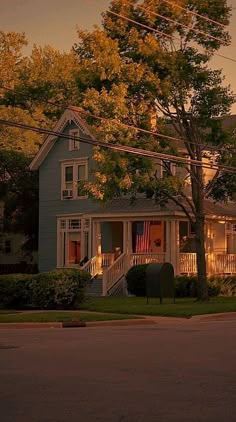 a blue house sitting on the side of a road next to a lush green tree