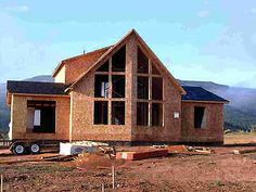 a house being built in the middle of a field with mountains in the back ground