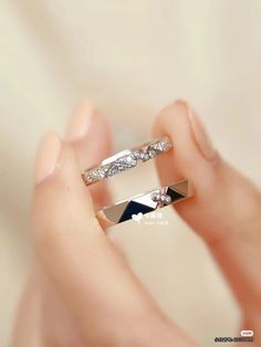 a woman's hand holding two wedding rings with diamond accents on each side and the other