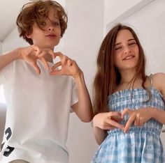 two young children standing next to each other with their hands in the shape of a heart