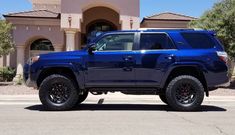 a blue toyota truck parked in front of a house with large tires on it's tires