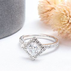 a white diamond ring sitting on top of a table next to a vase with flowers