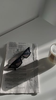 a newspaper with sunglasses on it next to a cup of coffee and a glass of beer