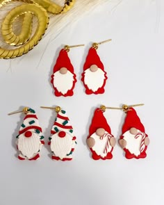 six santa claus earrings on a white table next to some gold and red decorations,