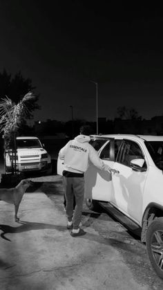 a black and white photo of a man standing in front of a car with his dog