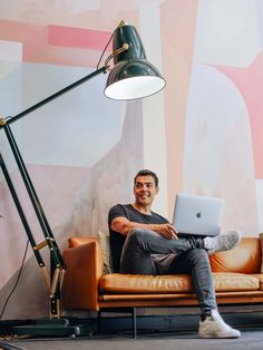 a man sitting on a couch with a laptop in front of him and a lamp next to him