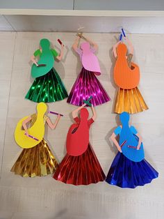 paper cut outs of women in colorful dresses hanging from hooks on a white wall with wooden planks