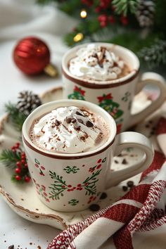 two cups filled with hot chocolate on top of a saucer next to a christmas tree