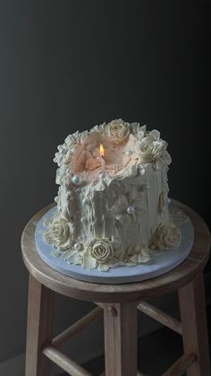 a white cake sitting on top of a wooden stool next to a wall with a lit candle in it