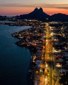 an aerial view of a city at night with mountains in the background and lights on