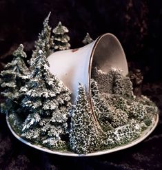 a white plate topped with snow covered evergreen trees and a silver bowl filled with pine cones