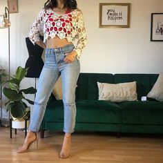 a woman standing in front of a green couch wearing jeans and a cropped top