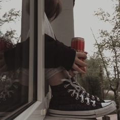 a person holding a drink in their hand while standing on a window sill outside