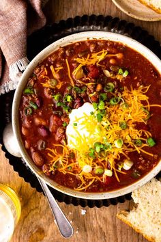 a bowl of chili with sour cream and cheese on top, next to some bread